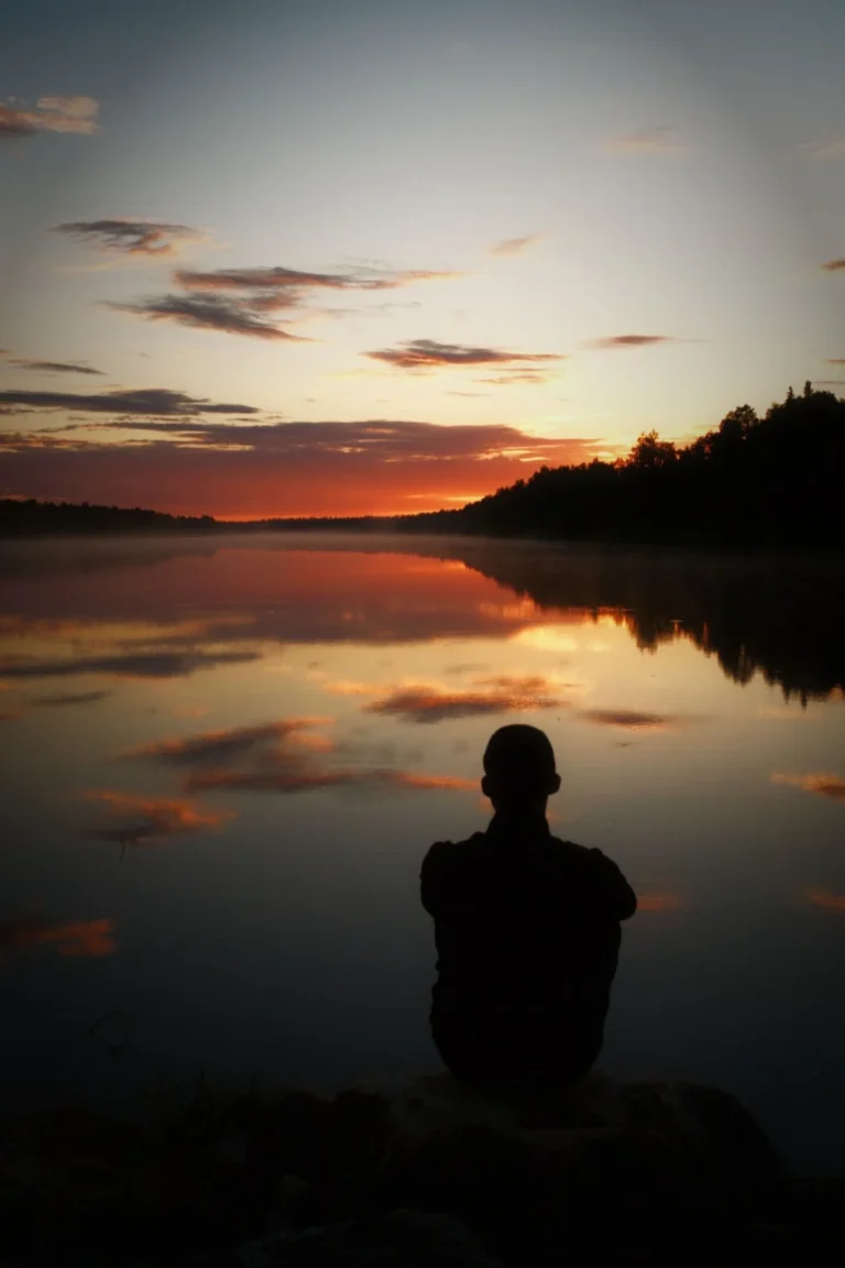 Person sitting alone by the water at sunset after a breakup