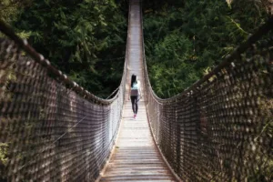 Woman walking alone across a suspension bridge in the woods