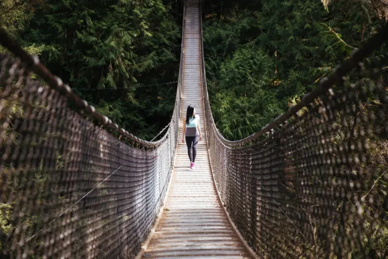 Woman walking alone across a suspension bridge in the woods