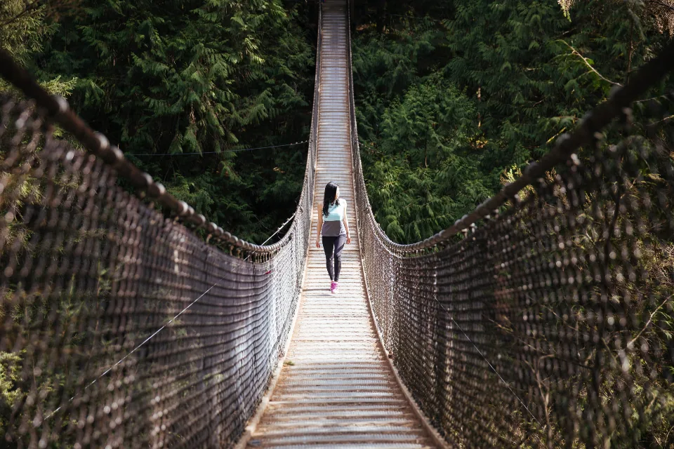 Woman walking alone across a suspension bridge in the woods